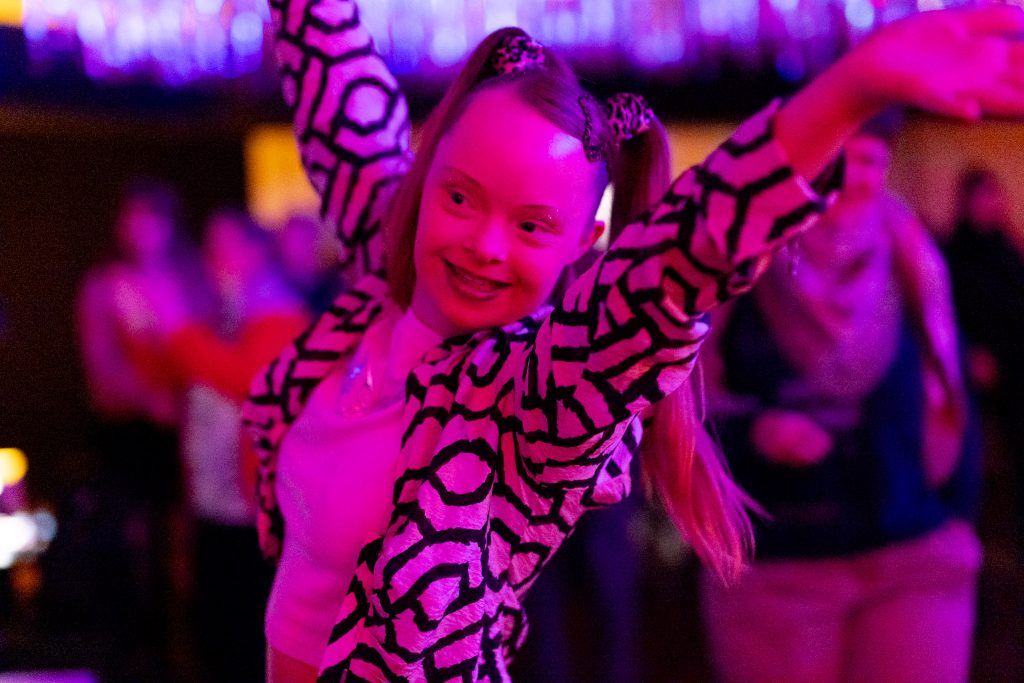 Eine Frau tanzt fröhlich unter pinkem Licht.