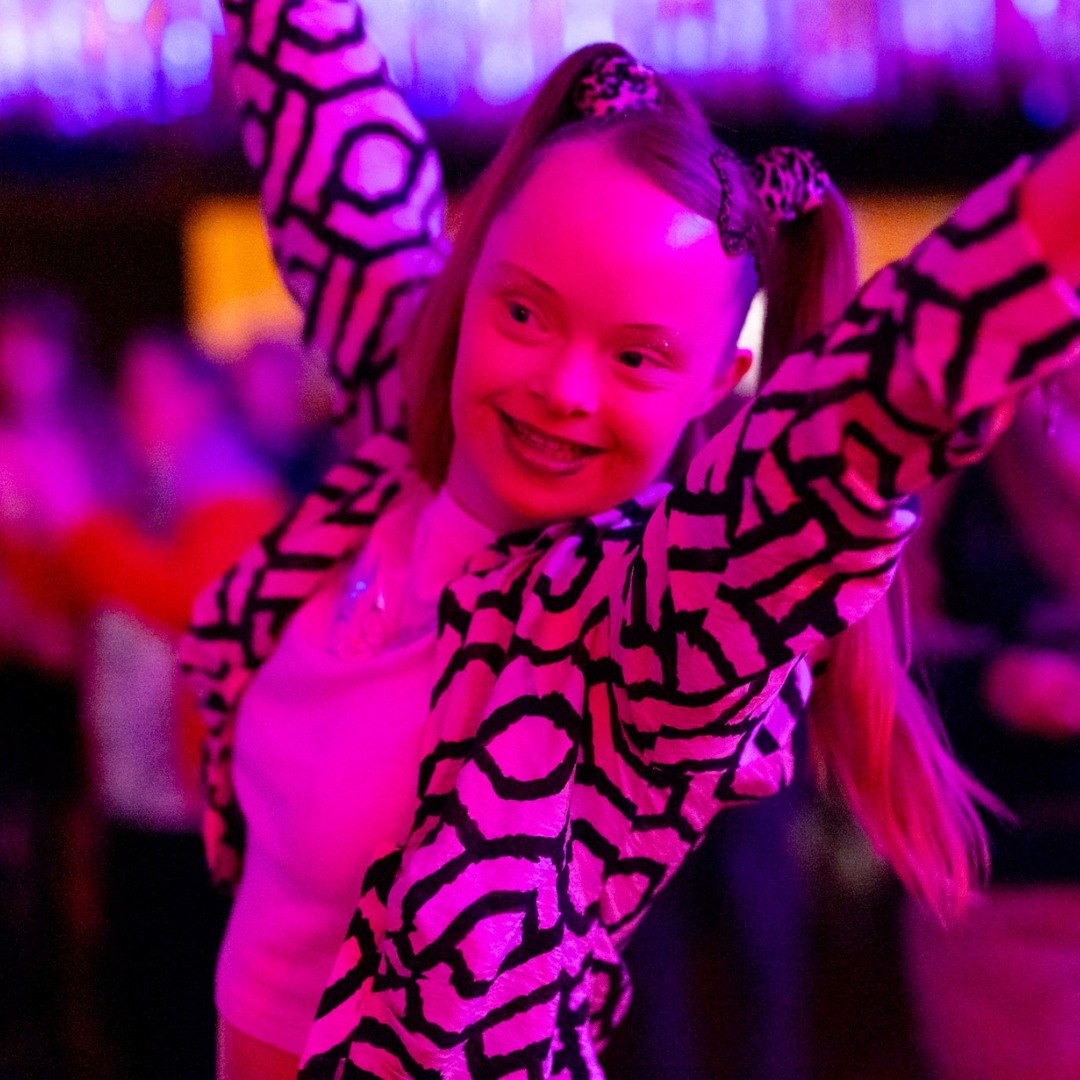 Eine Frau tanzt fröhlich unter pinkem Licht.